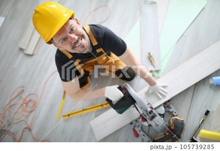 Builder in overalls and hard hat cut laminate on machine in room. 105739285