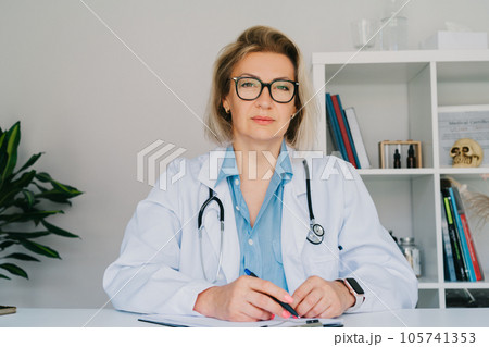 Portrait of confident mature middle aged woman doctor medical nurse portrait, female physician practitioner in white coat with stethoscope sitting at her working place at hospital office. 105741353