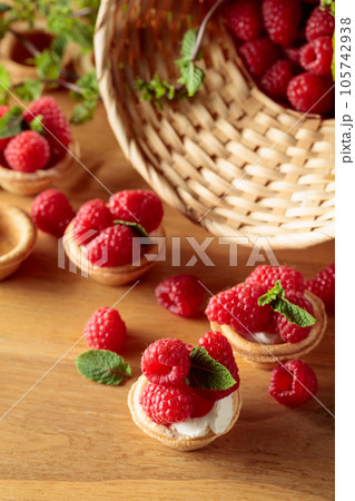 Tartlets with fresh raspberries and mint on a wooden table. Tartlets with fresh raspberries and mint on a wooden table. 105742938