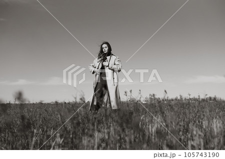Black and white photo of Young woman stands in dry grass reeds field looking away. Nature, vacation. 105743190