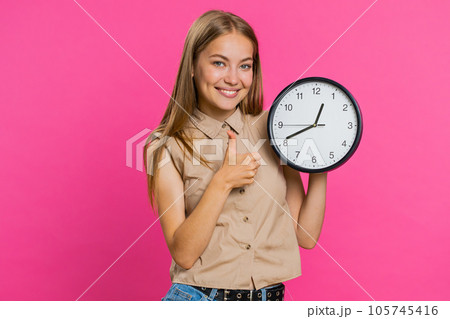 Woman showing time on wall office clock, ok, thumb up, approve, pointing finger at camera, your time Woman showing time on wall office clock, ok, thumb up, approve, pointing finger at camera, your time 105745416