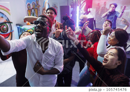 Happy friends group posing for selfie together while having fun and relaxing at nightclub party. Cheerful young diverse people crowd screaming and laughing while taking photo on dancefloor Happy friends group posing for selfie together while having fun and relaxing at nightclub party. Cheerful young diverse people crowd screaming and laughing while taking photo on dancefloor 105745476