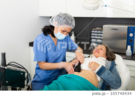 Cosmetologist performing abdominal skin rf lifting for aged woman Cosmetologist performing abdominal skin rf lifting for aged woman 105748434