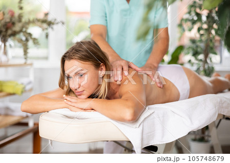 Relaxed middle-aged woman having back massage therapy conducted by skilled masseur 105748679