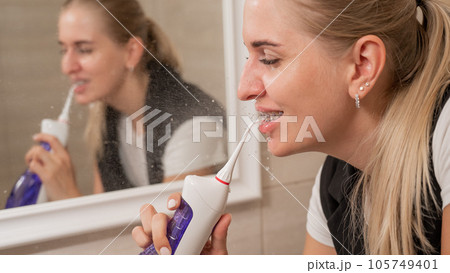 A woman with braces on her teeth uses an irrigator. Close-up portrait.  105749401
