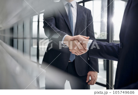 executives shaking hands in front of their manager and a colleague 105749686