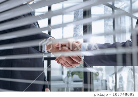 executives shaking hands in front of their manager and a colleague 105749695