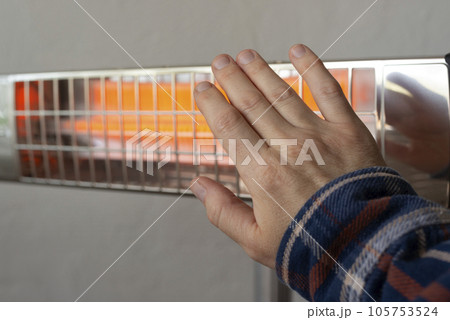 Caucasian male warming up hand near infrared heater Caucasian male warming up hand near infrared heater 105753524