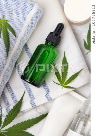 Green glass dropper bottle near green cannabis leaves top view, CBD cosmetic mockup Green glass dropper bottle near green cannabis leaves top view, CBD cosmetic mockup 105756513