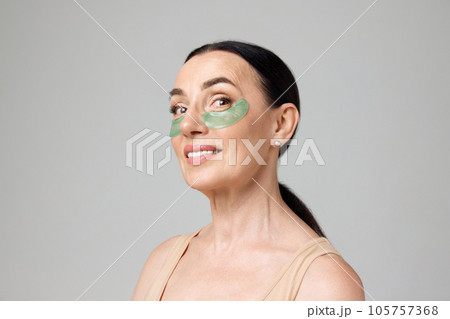 Portrait with mature woman using eye patches to get rid of eyes dark circles over grey background. Morning beauty routine 105757368