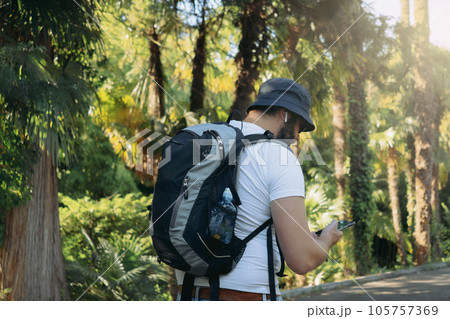 millenial bearded tourist man wearing bucket hat, with backpack and earpods using smartphone for navigation 105757369