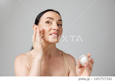Smiling senior woman applying anti-aging cream to hide wrinkles below eyes. Beauty skin care in old age. Smiling senior woman applying anti-aging cream to hide wrinkles below eyes. Beauty skin care in old age. 105757392