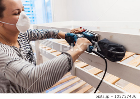 man rubs wooden child bed with power sander or grinder removing old paint 105757436