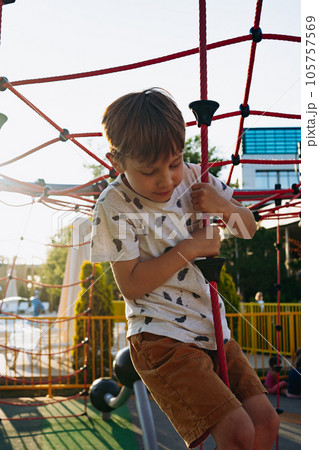 cute caucasian boy climbing a rope. Exercises on the playground. Selective focus on kid and backlight cute caucasian boy climbing a rope. Exercises on the playground. Selective focus on kid and backlight 105757569