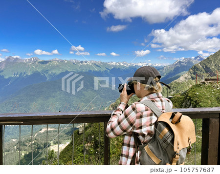 young stylish photographer woman taking photo of mountains standing at scenic viewpoint at Rosa peak, Sochi, Russia 105757687