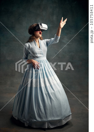 Portrait of surprised aristocratic woman wearing blue historical dress and VR glasses waving hand in air. Gadgets. Queen of technologies. Portrait of surprised aristocratic woman wearing blue historical dress and VR glasses waving hand in air. Gadgets. Queen of technologies. 105758411