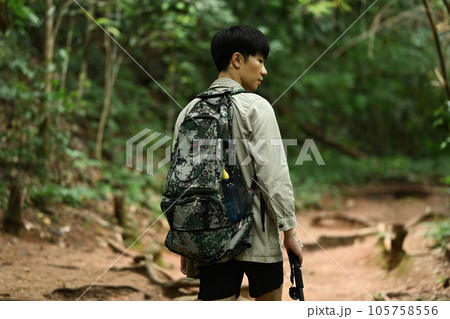 Back view of male hiker with backpack and trekking sticks trekking in forest. Travel, adventure and active life concept 105758556
