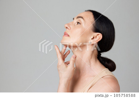 Profile photo mature woman touching skin on neck over light grey background. Copy space for ad 105758588