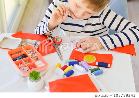 Close-up of a beautiful 9-year-old Caucasian boy who studies to sew with a needle and thread. Close-up of a beautiful 9-year-old Caucasian boy who studies to sew with a needle and thread. 105759243