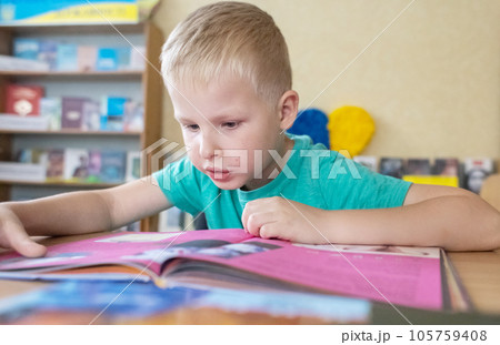 Boy in library. Seven year Ukrainian guy is sitting at a table in library and reading book. Concept of normal learning, thirst for knowledge, desire to learn new things. Blurred background and letters Boy in library. Seven year Ukrainian guy is sitting at a table in library and reading book. Concept of normal learning, thirst for knowledge, desire to learn new things. Blurred background and letters 105759408