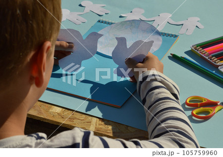 A close-up of the hands of a child who makes a postcard for the International Day of peace, crafts with his own hands, do it yourself, what to do with children. 105759960