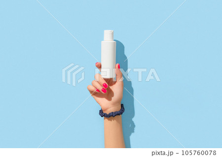 Womans hand holding white cream bottle on blue background. Body care beauty treatment concept Womans hand holding white cream bottle on blue background. Body care beauty treatment concept 105760078