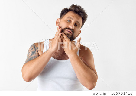 Attractive, bearded man taking care after beard with cosmetics, applying gel, wax, oil against white studio background 105761416