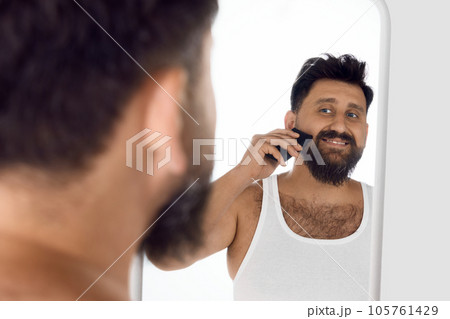 Mature, smiling man looking in mirror, taking care after beard, shaving with shaver against white studio background. Mature, smiling man looking in mirror, taking care after beard, shaving with shaver against white studio background. 105761429