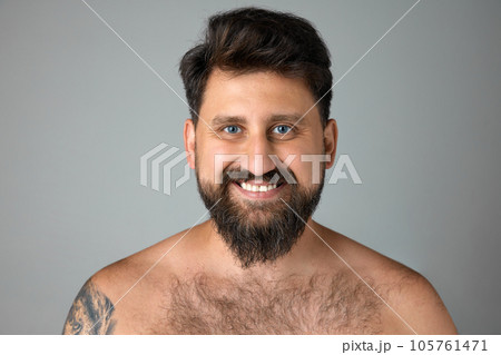 Smiling, mature, bearded man with blue eyes standing shirtless, looking at camera against grey studio background 105761471