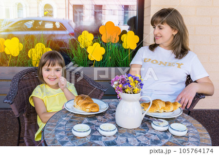 The happy girl has breakfast with mother in cafe on the street The happy girl has breakfast with mother in cafe on the street 105764174