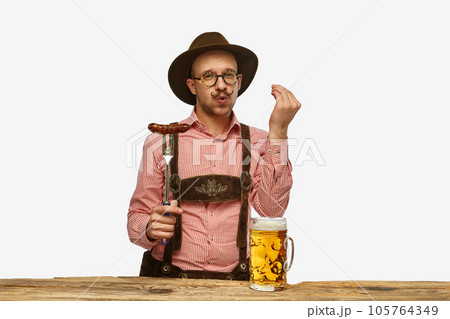 Delicious. Young man wearing traditional fest Bavarian or German outfit with big beer glass and fried sausage celebrating Oktoberfest. 105764349