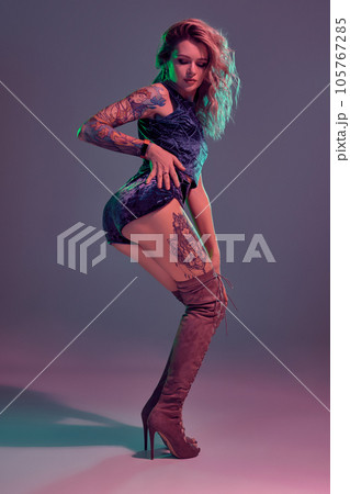 Attractive young blonde girl in blue velour booty shorts and maroon suede high boots posing on camera in studio Attractive young blonde girl in blue velour booty shorts and maroon suede high boots posing on camera in studio 105767285
