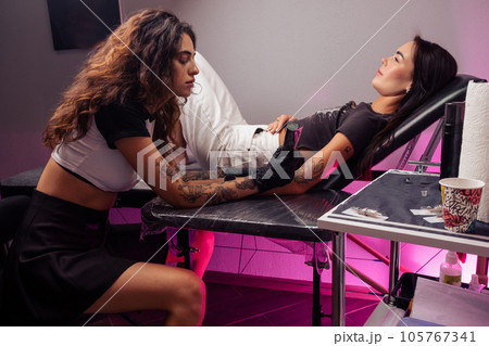 Female tattoo artist making colorful tattoo for girl in salon 105767341