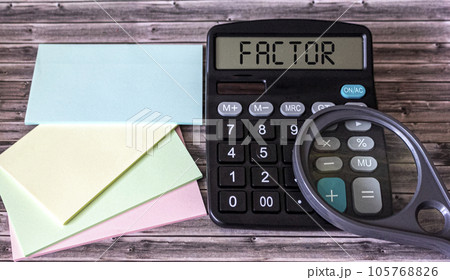 Text factor on a calculator, next to colored stickers and magnifier. Wood background Text factor on a calculator, next to colored stickers and magnifier. Wood background 105768826