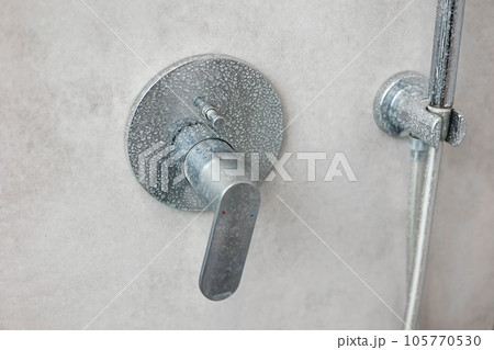 Dirty calcified shower mixer tap, faucet with limescale on it, plaque from hard water, Chrome plated shower, close up photo. Bathroom with grey tiles interior. 105770530