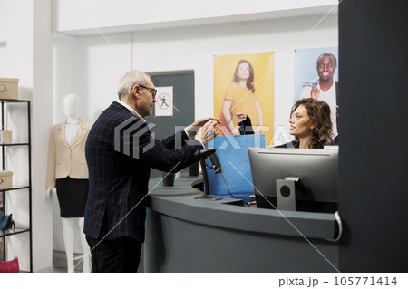 Senior customer taking shopping bag from boutique worker, after buying fashionable clothes in shopping centre. Elderly shopper paying for stylish merchandise during commercial activity 105771414