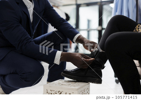 Retail employee helping african american client with purchase in shopping center. Stylish customer trying stylish shoes, buying trendy merchandise in boutique, commercial activity. Close up Retail employee helping african american client with purchase in shopping center. Stylish customer trying stylish shoes, buying trendy merchandise in boutique, commercial activity. Close up 105771415
