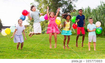 Barefoot children with balloons jumping on grass 105773803