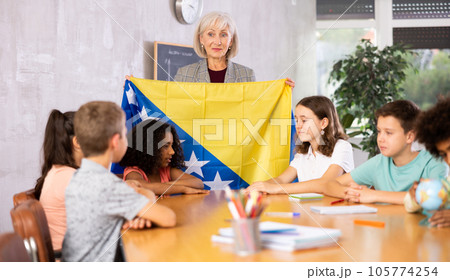 Female teacher showing bosnian flag to kids in geography class Female teacher showing bosnian flag to kids in geography class 105774254