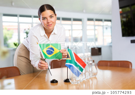 Young lady sets miniatures flags of South Africa and Brazil for international negotiations 105774293