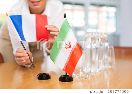 Little flag of Iran on table and flag of France put next to it by young woman Little flag of Iran on table and flag of France put next to it by young woman 105774309