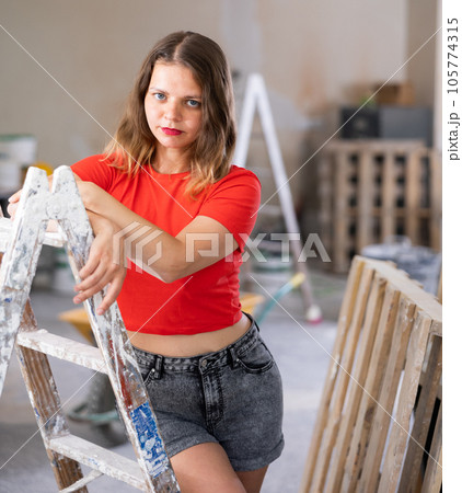 Playful woman in red t-shirt and denim shorts posing in refurbished room 105774315