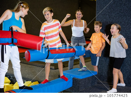 Happy child school boy and teenage girl friends fighting by inflatable logs while spending weekend together in entertainment center 105774425