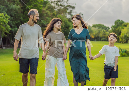 A loving family enjoying a leisurely walk in the park - a radiant pregnant woman after 40, embraced by her husband, and accompanied by their adult teenage children, savoring precious moments together 105774508