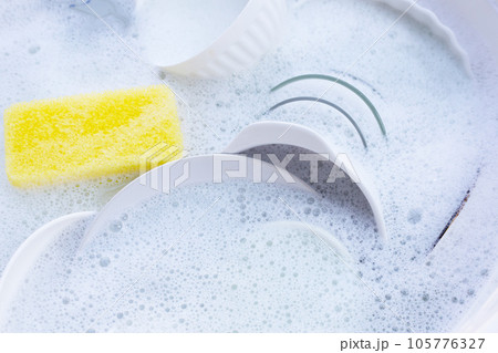 Dishes and bowls with yellow sponge in water and bubbles of dishwashing liquid Dishes and bowls with yellow sponge in water and bubbles of dishwashing liquid 105776327