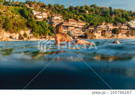 Surfer rowing on a surfboard in ocean with coastline landscape on Bali. Surfer rowing on a surfboard in ocean with coastline landscape on Bali. 105780267