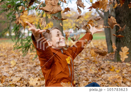 The boy throws autumn yellow leaves that fly at him The boy throws autumn yellow leaves that fly at him 105783623