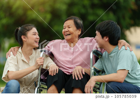 happy grandson and granddaughter talking with senior woman in wheelchair at park happy grandson and granddaughter talking with senior woman in wheelchair at park 105785039