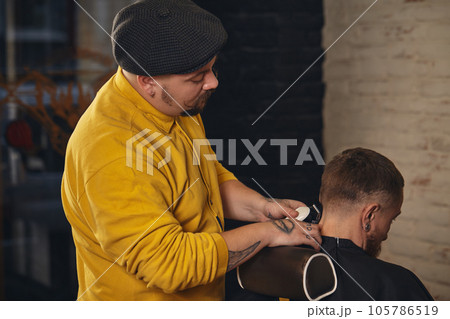 Barber making haircut of attractive bearded man in barbershop Barber making haircut of attractive bearded man in barbershop 105786519