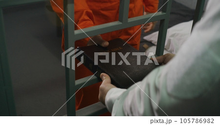 Prison officer gives Bible to male prisoner in orange uniform Prison officer gives Bible to male prisoner in orange uniform 105786982